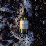 ANGAN Volcanic Glow Body Oil — lifestyle shot at golden hour on the beach